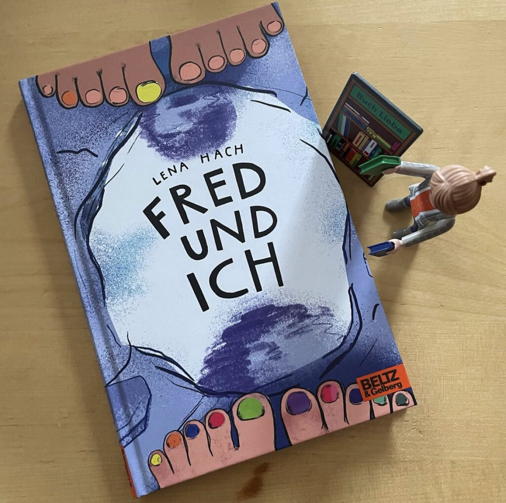 Das Buch "Fred und ich" liegt auf einem Tisch. Daneben steht die Playmobilfigur einer Buchhändlerin.