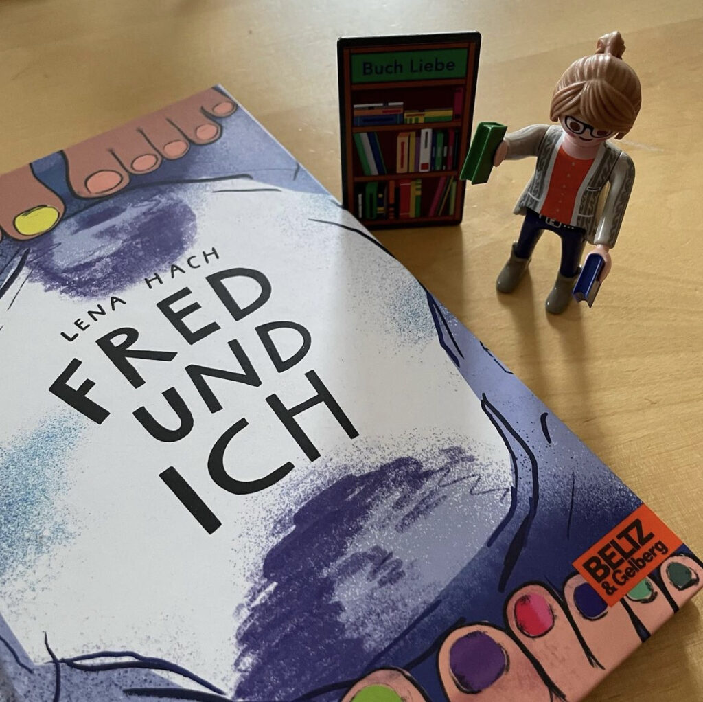 Das Buch "Fred und ich" liegt auf einem Tisch. Daneben steht die Playmobilfigur einer Buchhändlerin.