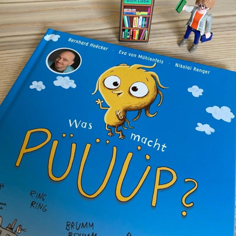 Das Buch "Was macht Püüüp?" liegt auf einem Holztisch. Das Buchcover liegt schief und ist angeschnitten. Neben dem Buch steht eine Playmobil-Figur - die Buchhändlerin.