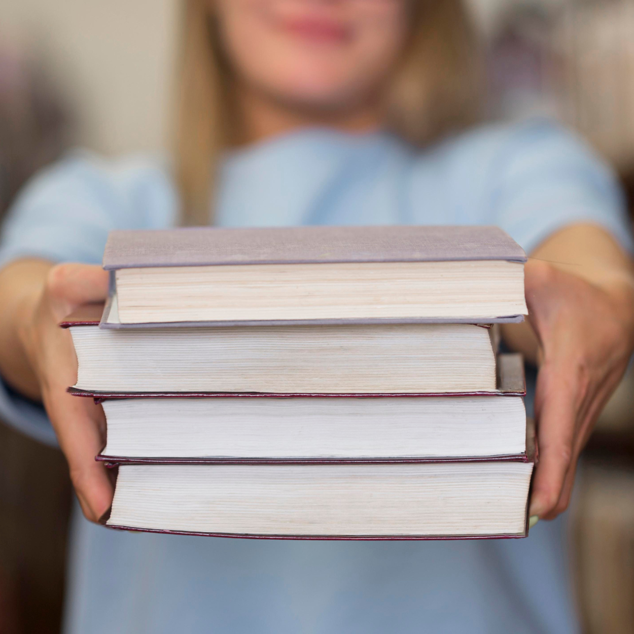 Person verschwommen im Hintergrund hält vier Bücher in die Kamera